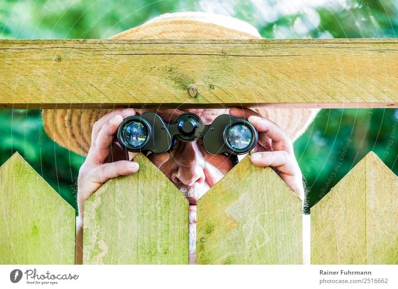 ein neugieriger Nachbar beobachtet mit einem Fernglas Mensch maskulin Mann Erwachsene Männlicher Senior 1 Natur Garten Park Hut Strohhut beobachten bedrohlich