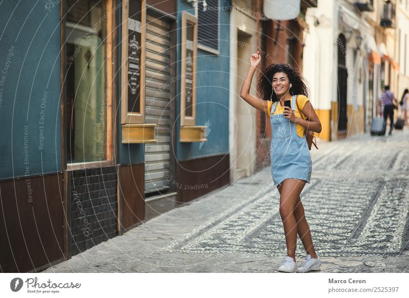 schönes gemischtes Mädchen, das der Musik lauscht und glücklich auf der Straße geht Afrikanisch Rucksack schwarz blau braune Haare lässig celular Farben