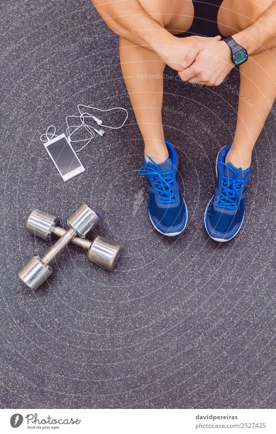 Sportlicher Mann sitzt mit Hanteln und Smartphone auf dem Boden des Fitnessstudios. Lifestyle Körper Freizeit & Hobby Musik Telefon PDA Mensch Erwachsene