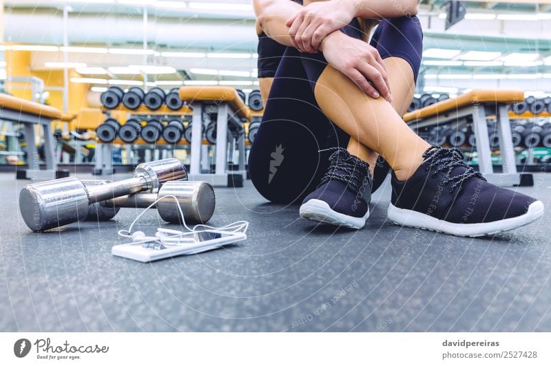 Sportliche Frau sitzt mit Hanteln und Smartphone auf dem Boden des Fitnessstudios. Lifestyle schön Körper Freizeit & Hobby Musik Telefon PDA Mensch Erwachsene