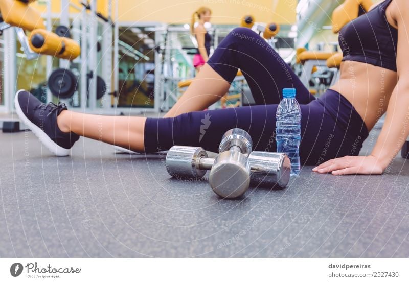 Frau, die sich ausruht und Freundin, die Kurzhantel-Übungen im Fitnessstudio macht. Flasche Lifestyle Glück schön Körper Freizeit & Hobby Club Disco Sport