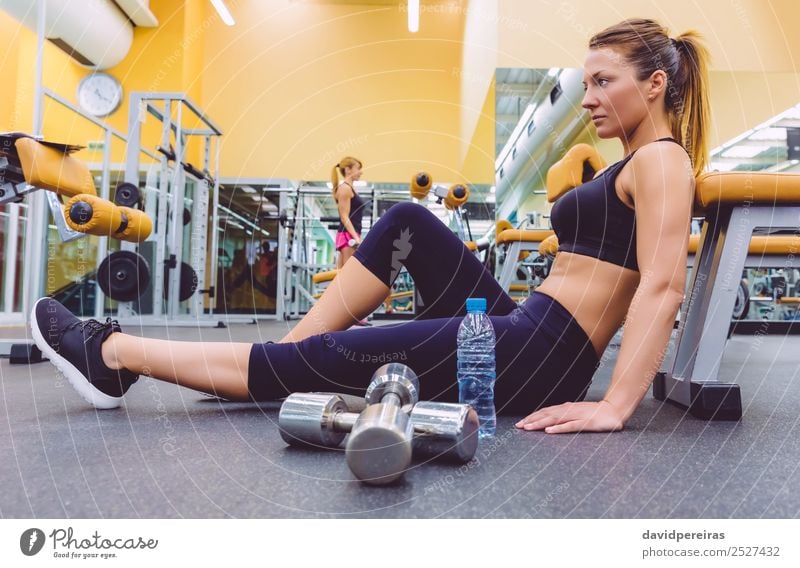 Frau, die sich ausruht und Freundin, die Kurzhantel-Übungen im Fitnessstudio macht. Flasche Lifestyle Glück schön Körper Freizeit & Hobby Club Disco Sport