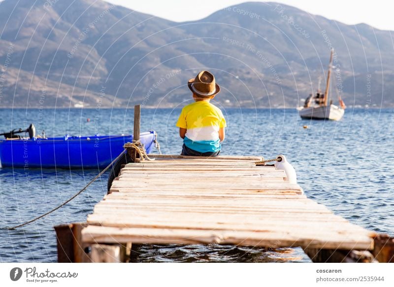 Kleiner Junge auf einem Dock, der auf dem Rücken sitzt und auf den Ozean schaut. Lifestyle Freude Glück Freizeit & Hobby Ferien & Urlaub & Reisen Sommer Strand