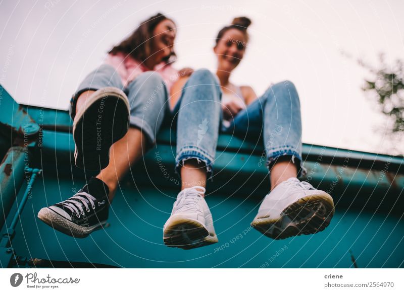 zwei freche Frauen, die auf einem großen Behälter sitzen. Lifestyle Freude Glück sprechen Mensch Erwachsene Freundschaft Jeanshose Turnschuh lachen lustig