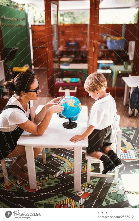 kleiner Junge, der mit der Lehrerin im Klassenzimmer studiert. Glück Schreibtisch Kind Schule Klassenraum Mensch Frau Erwachsene Mann Buch Globus sitzen