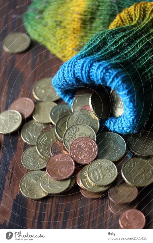 gestrickte bunte Wollsocke als Sparstrumpf mit Geldmünzen auf einem Holztisch Strümpfe Euro Cent liegen Armut außergewöhnlich klein rund braun gelb grün