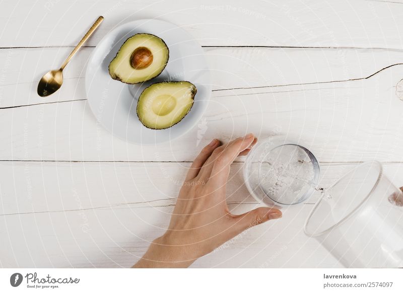 Flache Schicht aus frisch geschnittenen, reifen Avocadohälften und Frau, die Wasser gießt. Hand Tasse Vegetarische Ernährung Vegane Ernährung flache Verlegung