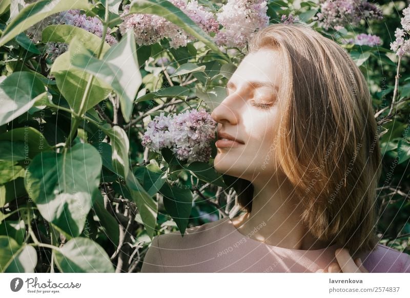 Lifestyle-Porträt einer jungen weißen Frau in fliederfarbenen Blumen aromatisch attraktiv schön Beautyfotografie Sträucher niedlich Gesicht Mode Junge Frau grün