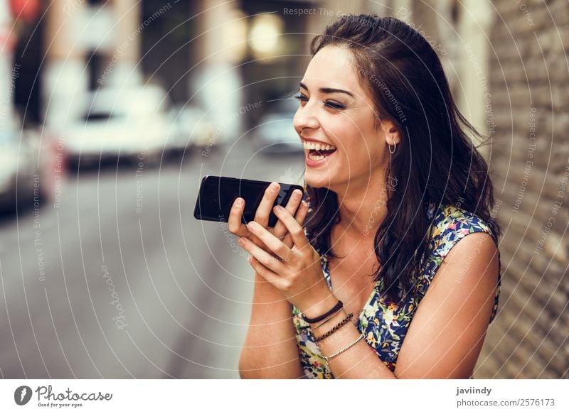 Lächelnde junge Frau, die im Freien mit ihrem Smartphone Sprachnotizen aufzeichnet. Lifestyle Stil Glück schön Haare & Frisuren Telefon PDA