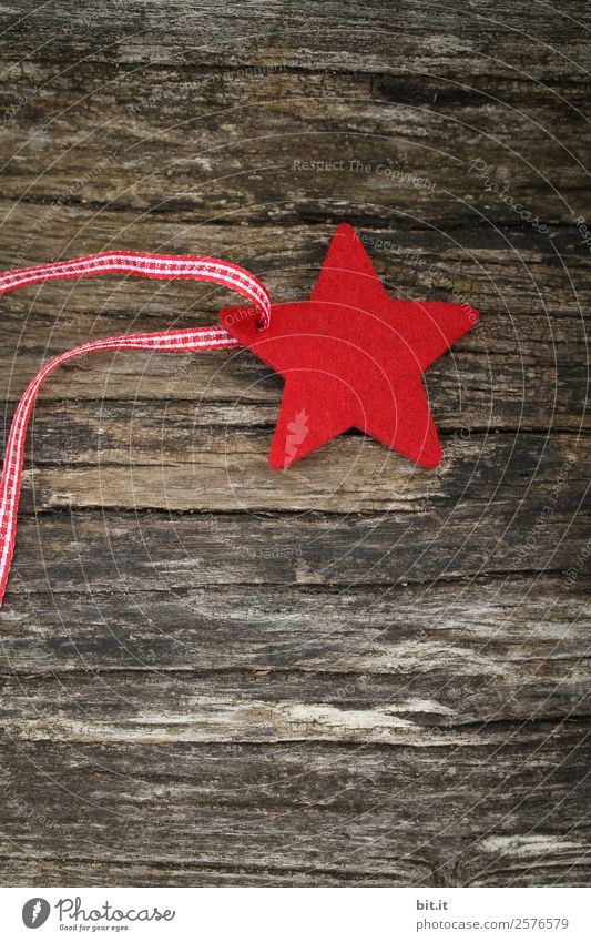 Frohe Weihnachten. Roter Stern aus Filz mit Band, liegt auf altem Holz. Roter Karo-Weihnachtsstern, als Dekoration auf rustikalem, braunen Holzbrett. Filz-Stoff-Stern als Schild, Blanko, Anhänger, Aufhänger auf braunem, rustikalem Holztisch, Textfreiraum.