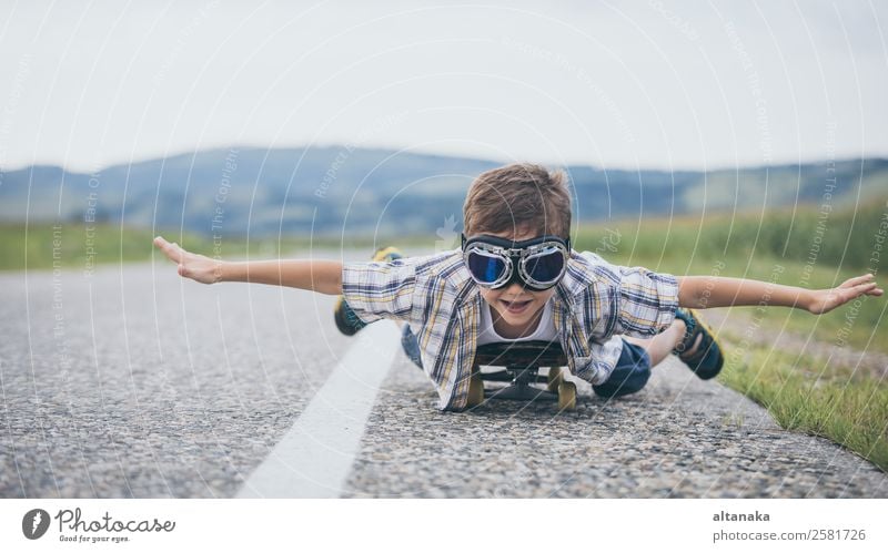 Fröhlicher kleiner Junge, der tagsüber auf der Straße spielt. Ein Kind, das Spaß im Freien hat. Er fährt Skateboard auf der Straße. Konzept des Sports.