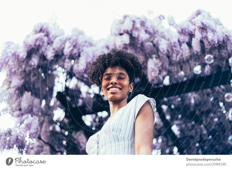 Fröhliche junge schwarze Frau, umgeben von Blumen. Lifestyle Glück schön Erholung Sommer Garten Erwachsene Natur Baum Blüte Kleid Sonnenbrille Lächeln