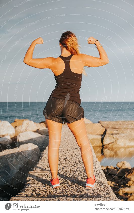 Junges Mädchen mit starkem Bizeps nach Fitnesstraining im Freien. Fitness-Frau. Ganzkörper-Rückenansicht. Freude Glück schön Körper Sommer Strand Sport Erfolg