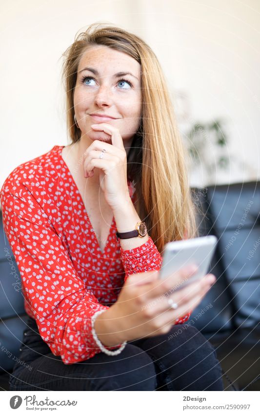 Schöne Frau, die das Handy benutzt und nachdenklich aussieht. Lifestyle Leben Wohnung Haus Sofa Wohnzimmer Telefon Headset PDA Technik & Technologie Jugendliche