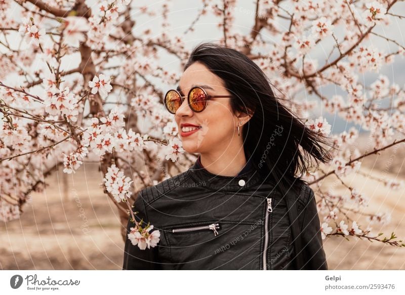 Hübsches brünettes Mädchen Stil Glück schön Gesicht Garten Mensch Frau Erwachsene Natur Baum Blume Blüte Park Mode Jacke Leder Sonnenbrille Lächeln Fröhlichkeit