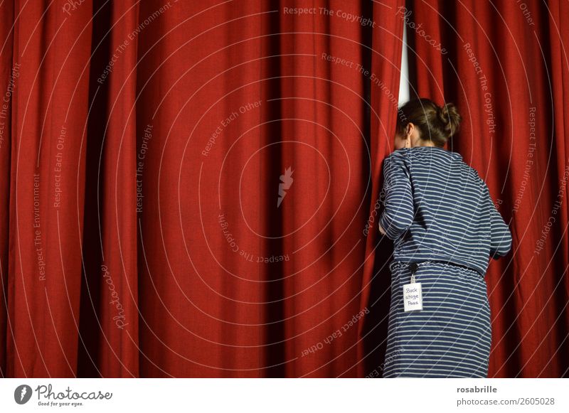 junge Frau in blauem Kleid wagt einen Blick hinter die Kulissen und schaut neugierig hinter einen roten Theatervorhang als Symbol für Hintergrundinfos, Einblicke oder Vorankündigungen