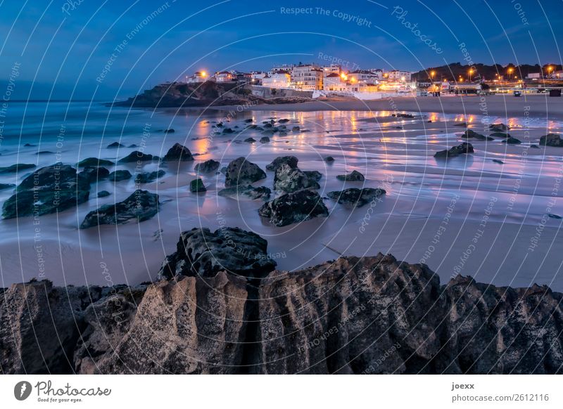 Felsen am Atlantik-Strand bei Niedrigwasser mit beleuchtetem Städtchen im Hintergrund bei Abenddämmerung Sommer Meer Portugal Praia das Maçãs