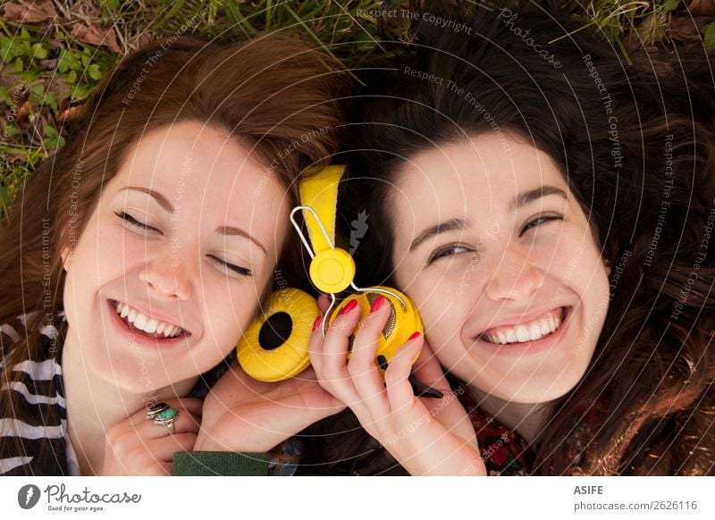 Teenagermädchen teilen Musik, die im Gras liegt. Freude schön Winter Headset Mensch Frau Erwachsene Freundschaft Jugendliche Herbst Blatt brünett blond