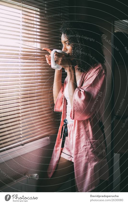 hübsche schwarze Frau am Fenster stehend mit einer Tasse Kaffee Tee hintergrundbeleuchtet Schlafzimmer Afro-Look Afroamerikaner genießen trinken Jugendliche