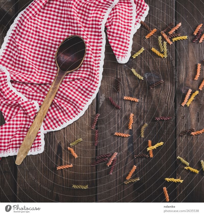 rohe Nudelnusilli auf einem braunen Holztisch Teigwaren Backwaren Ernährung Diät Löffel gelb rot Farbe Tradition farbenfroh Essen zubereiten Speise trocknen