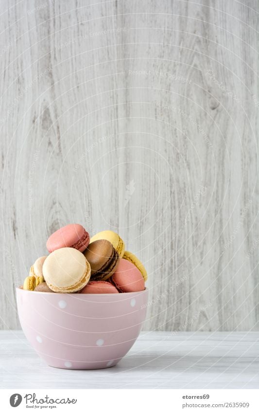 Bunte Makronen in einer Schleife auf weißem Holztisch Macaron Erdbeeren Zitrone Dessert Kaffee gelb Schokolade Konfekt Himbeeren Tradition Süßwaren