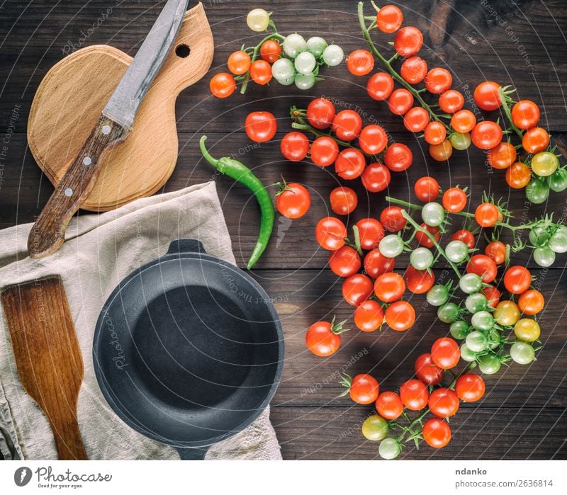 gusseiserne runde Bratpfanne und reife rote Kirschtomaten Gemüse Kräuter & Gewürze Vegetarische Ernährung Topf Messer Tisch Küche Holz Essen frisch klein