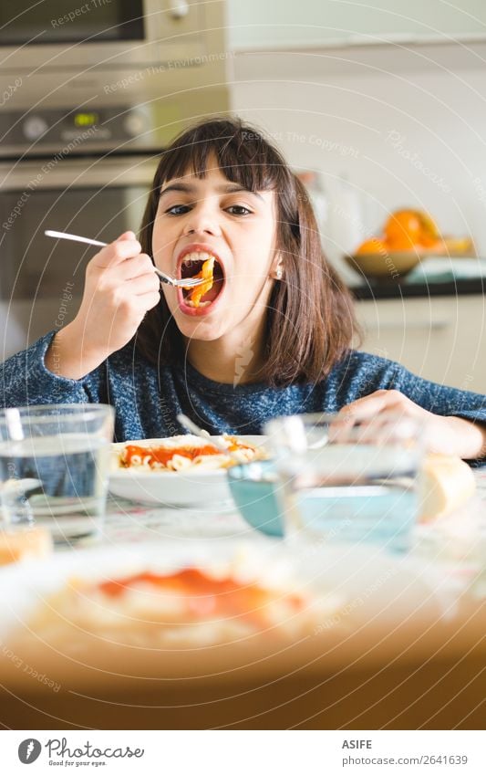 Nettes und glückliches kleines Mädchen isst Nudeln mit Tomatensauce und Käsepulver in der Küche zu Hause Ernährung Essen Mittagessen Abendessen Gabel Freude