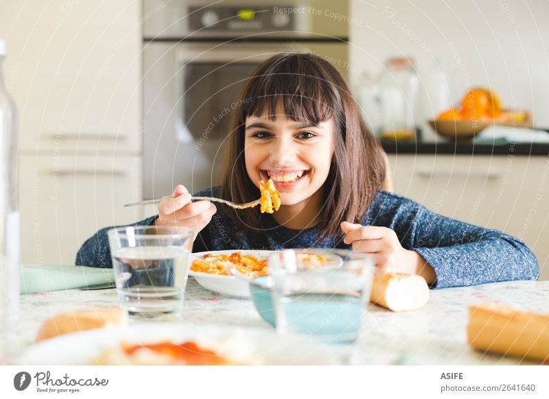 Nettes und glückliches kleines Mädchen isst Nudeln mit Tomatensauce und Käsepulver in der Küche zu Hause Ernährung Essen Mittagessen Abendessen Gabel Freude