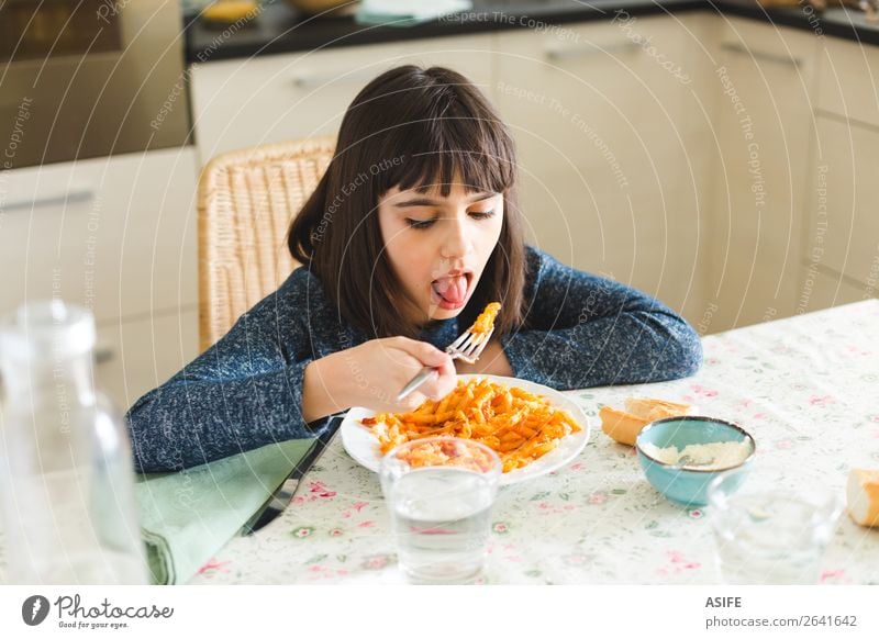 Nettes und glückliches kleines Mädchen isst Nudeln mit Tomatensauce und Käsepulver in der Küche zu Hause Ernährung Essen Mittagessen Abendessen Gabel Freude