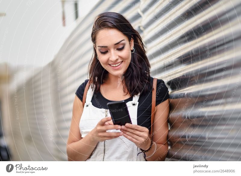 Lächelnde junge Frau, die ihr Smartphone im Freien benutzt. Glück schön Haare & Frisuren Telefon PDA Technik & Technologie Mensch feminin Junge Frau Jugendliche