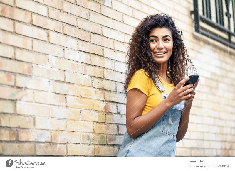 Glückliches arabisches Mädchen mit Smartphone an der Ziegelwand. Lifestyle Stil schön Haare & Frisuren Telefon PDA Technik & Technologie Mensch feminin