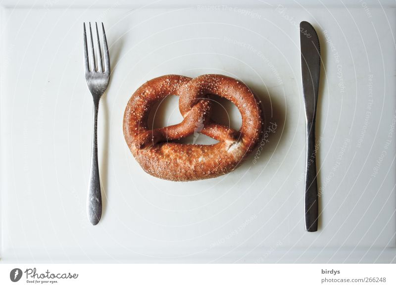 Laugenbrezel mit Messer und Gabel auf weißem Untergrund. Brezel Ernährung ästhetisch einfach lustig braun silber 1 3 Besteck deutsche Backwaren minimalistisch