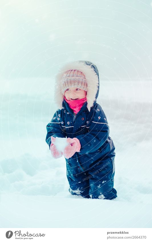 Fröhliches kleines Mädchen genießt den Schnee. Kind, das draußen spielt und im Winter bei Schneefall durch tiefen Schnee läuft. Kleinkind trägt dunkelblauen Schneeanzug