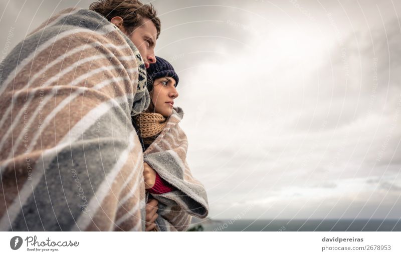 Junges Paar unter der Decke, das an einem kalten Tag auf das Meer schaut. Lifestyle Glück schön Winter Berge u. Gebirge Frau Erwachsene Mann Natur Himmel Wolken