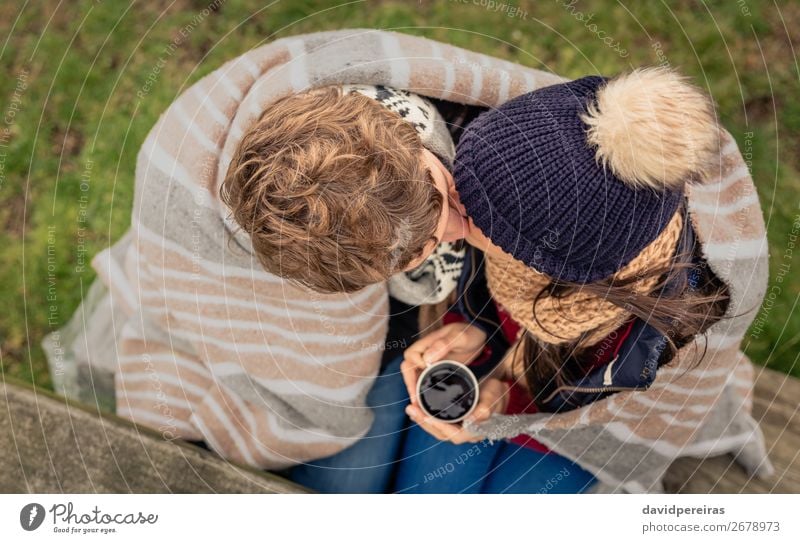 Junges Paar unter der Decke mit heißem Getränk, das sich im Freien küsst. Kaffee Tee Lifestyle Abenteuer Winter Tisch Frau Erwachsene Mann Hand Natur Herbst