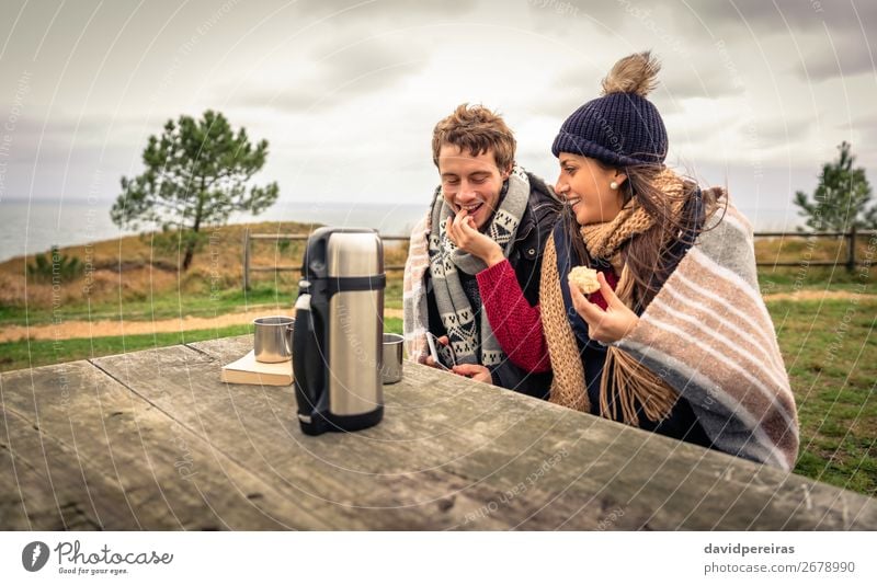 Junges Paar unter der Decke isst Muffin im Freien an einem kalten Tag. Essen Getränk Kaffee Lifestyle Glück Meer Winter Tisch Frau Erwachsene Mann Natur Himmel