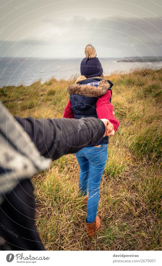 Junge Frau, die die Hand des Mannes hält und von einer Wiese führt. Lifestyle Glück schön Meer Winter Erwachsene Paar Natur Himmel Wolken Herbst Wind Küste