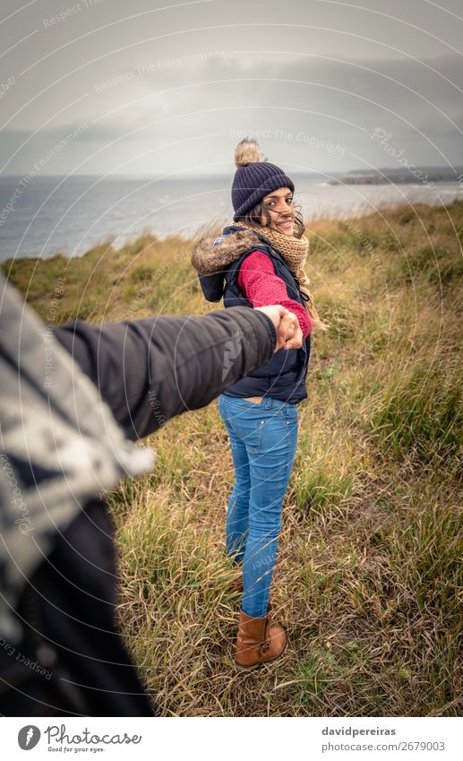 Junge Frau, die die Hand des Mannes hält und von einer Wiese führt. Lifestyle Glück schön Meer Winter Erwachsene Paar Natur Himmel Wolken Herbst Wind Küste