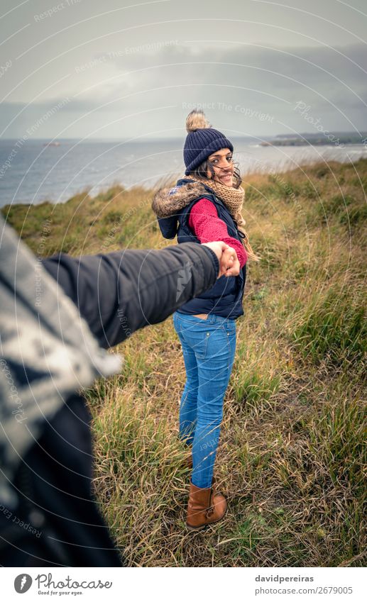 Junge Frau, die die Hand des Mannes hält und von einer Wiese führt. Lifestyle Glück schön Abenteuer Meer Winter Erwachsene Paar Natur Himmel Wolken Herbst Wind