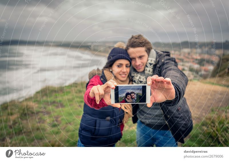 Junges Paar beim Fotografieren mit dem Smartphone im Freien Glück Abenteuer Strand Meer Winter Telefon PDA Frau Erwachsene Mann Natur Landschaft Himmel Wolken