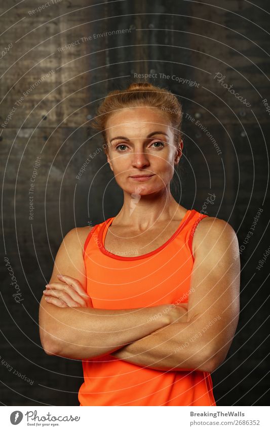 Close up vorderen Oberkörper Porträt eines jungen sportlichen Frau in Sportkleidung in der Turnhalle über dunklen Hintergrund, Blick auf die Kamera und lächelnd