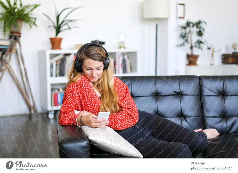 Junge Frau benutzt ein Smartphone und hört Musik, während sie auf einer Ledercouch liegt Lifestyle Freude Glück schön Haare & Frisuren Erholung Windstille