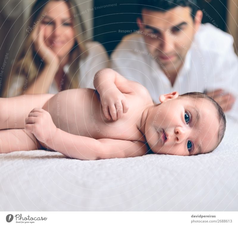 Neugeborenes liegt über dem Bett und das Paar lächelt auf dem Hintergrund. Lifestyle Freude Glück schön Freizeit & Hobby Schlafzimmer Kind Mensch Baby Kleinkind