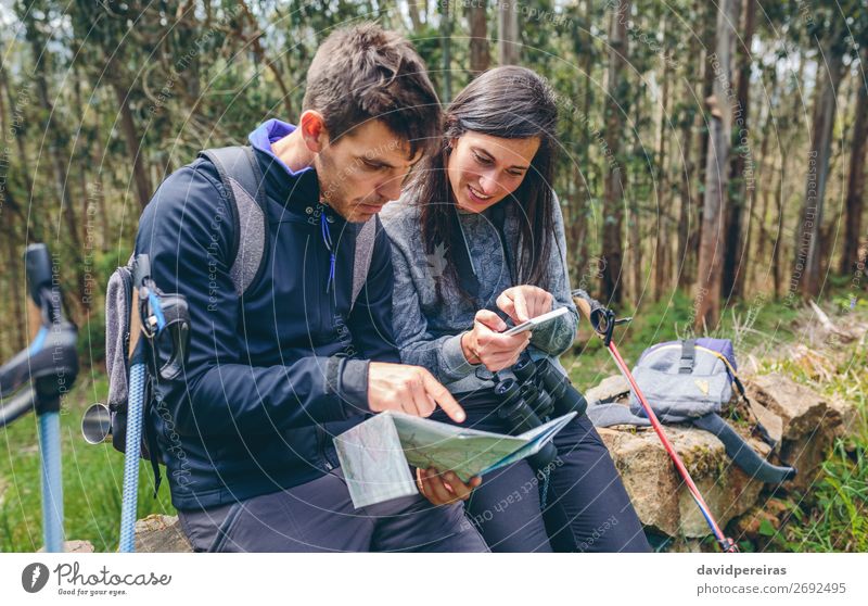 Ein Paar beim Trekking im Sitzen, das mobil aussieht und eine Karte hat. Ausflug Abenteuer Sightseeing Berge u. Gebirge wandern Sport PDA Mensch Frau Erwachsene