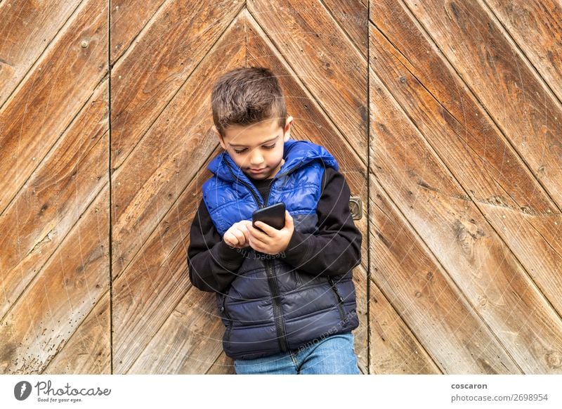 Kleiner Junge mit einem beweglichen Telefon mit einem Hintergrund aus Holztüren. Lifestyle schön Spielen Ferien & Urlaub & Reisen Haus Kind Handy PDA