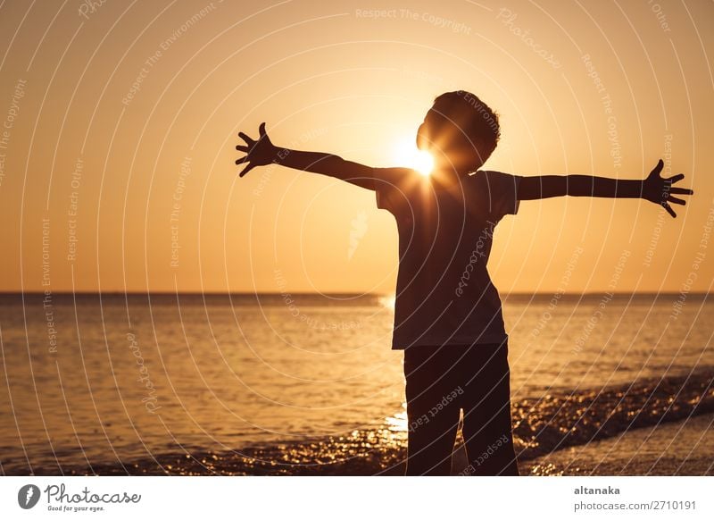 Ein glücklicher kleiner Junge, der zur Zeit des Sonnenuntergangs am Strand spielt. Ein Kind, das Spaß im Freien hat. Konzept der Sommerferien. Lifestyle Freude