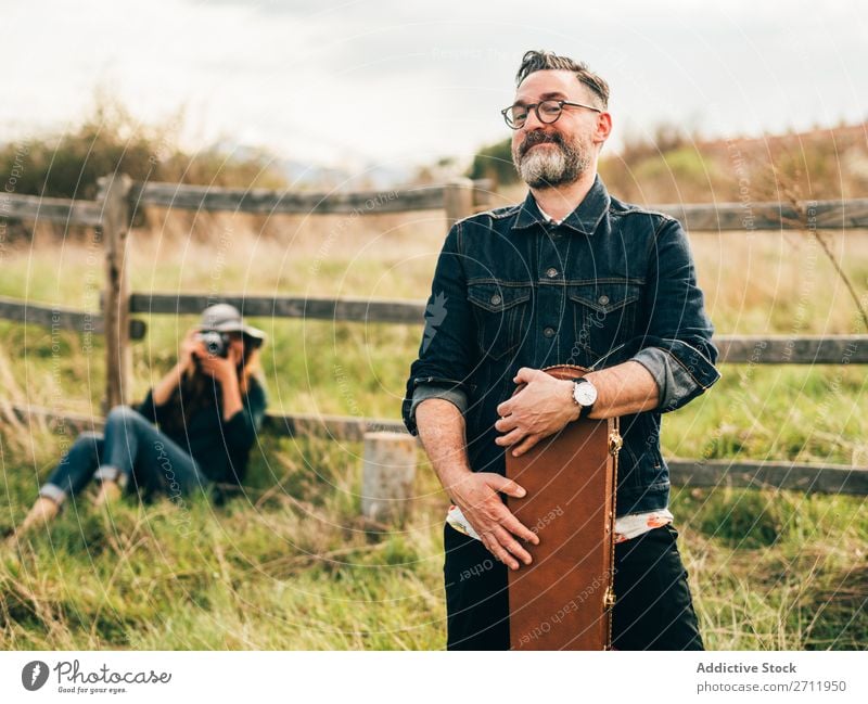 Frau, die mit der Gitarre einen Mann fotografiert. Natur Musiker Fotograf fallen sitzen ländlich Zaun Lifestyle Mensch Sommer lässig akustisch gutaussehend Typ