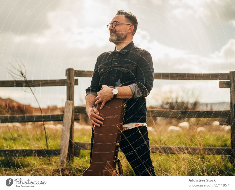 Erwachsener Mann mit Gitarrenkoffer Natur Musiker fallen stehen Wegsehen ländlich Zaun Lifestyle Mensch Sommer lässig akustisch gutaussehend Typ