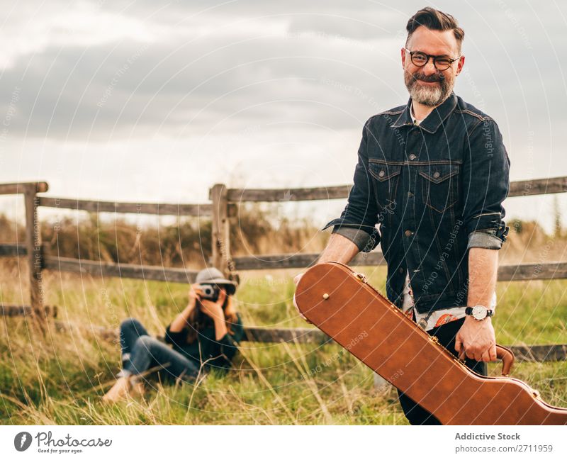 Frau, die mit der Gitarre einen Mann fotografiert. Natur Musiker Fotograf fallen sitzen ländlich Zaun Lifestyle Mensch Sommer lässig akustisch gutaussehend Typ