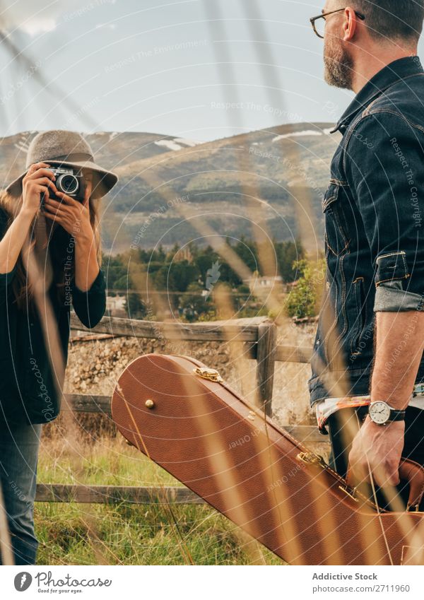 Frau, die mit der Gitarre einen Mann fotografiert. Natur Musiker Fotograf fallen ländlich Zaun Lifestyle Mensch Sommer lässig akustisch gutaussehend Typ